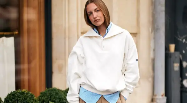 Frau kombiniert lässig ein gestreiftes Hemd mit einem weißen Pullover, der wie ein Hoodie wirkt.