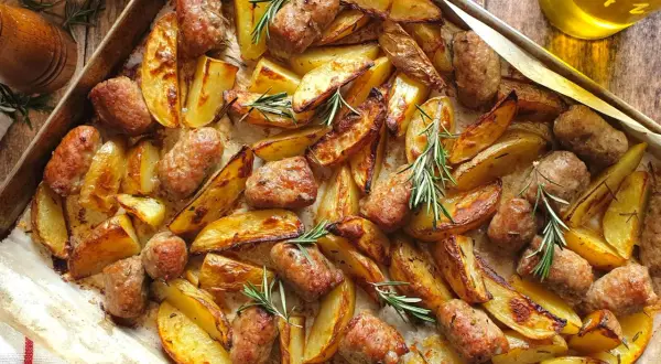 Salsiccia e patate al forno, dorate e profumate al rosmarino, pronte per essere gustate.