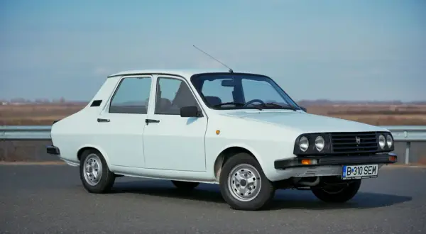 Biała Dacia 1300 stoi na drodze, gotowa na podróż. Klasyczny design i proste linie tego samochodu przyciągają wzrok.
