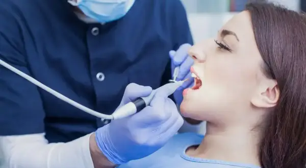 Dentysta bada zęby pacjentki. Zastanawiasz się, ile kosztuje wizyta u dentysty?