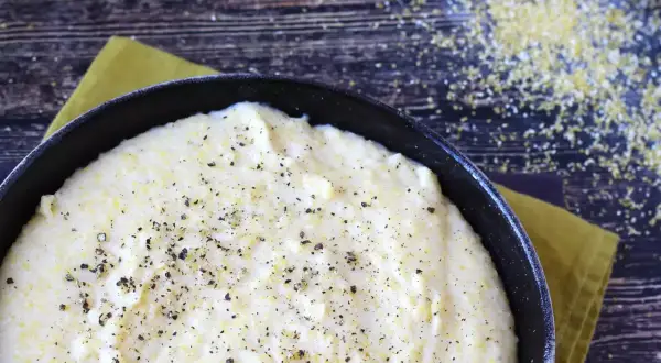 Kremowa polenta w czarnej patelni, posypana świeżo mielonym pieprzem, na drewnianym tle.