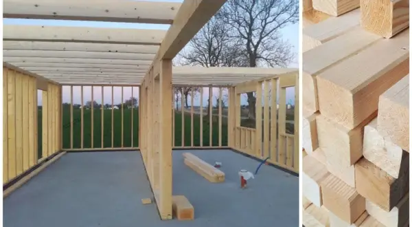 Budowa domu z drewna. Widok wnętrza konstrukcji szkieletowej z belkami stropowymi i ścianami. Obok stosy desek, pokazujące, co to jest drewno budowlane.