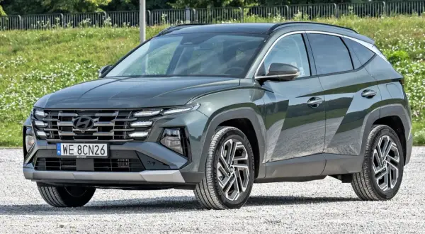 Nowy, tani SUV Hyundai Tucson w ciemnozielonym kolorze, zaparkowany na żwirowej drodze.