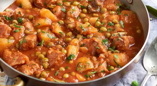 Un saporito spezzatino di vitello con piselli e patate, cotto in un sugo rosso e guarnito con prezzemolo fresco.