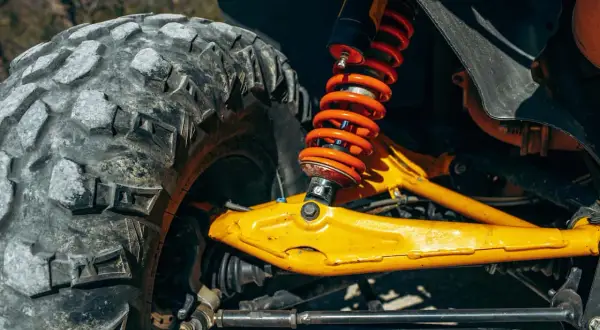 Gros plan sur la jambe de force voiture, avec son amortisseur orange vif et son pneu tout-terrain. Le bras de suspension jaune vif est prêt pour l'aventure.