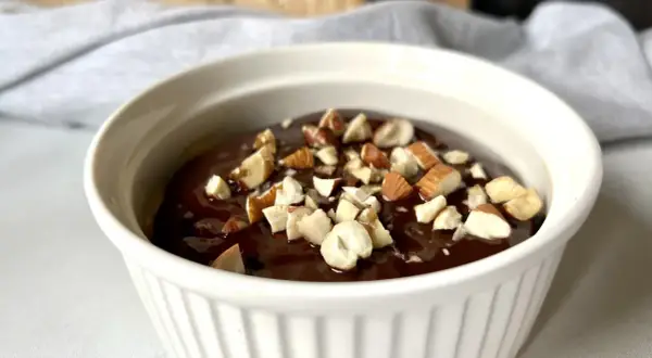 Czekoladowy deser low carb posypany orzechami w białej miseczce.