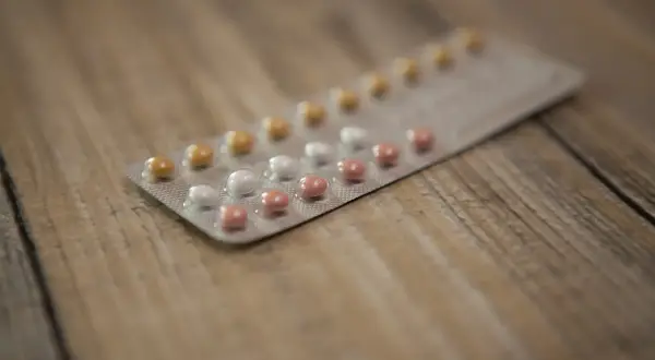 Opakowanie tabletek antykoncepcyjnych z kilkoma rzędami tabletek w różnych kolorach, leżące na drewnianym blacie.