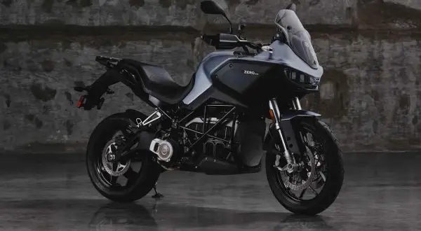 Motocicleta eléctrica Zero DSR/X, con potencia de 35kW, color gris oscuro, sobre suelo mojado y fondo de pared de ladrillo.