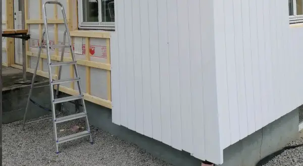 Byggarbetsplats där man valt att kombinera liggande och stående panel på husfasaden. En stege står redo.