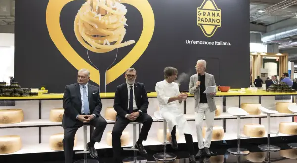 Män sitter på stolar framför en stor vägg med en bild av pasta och texten "GRANA PADANO. Un'emozione italiana.
