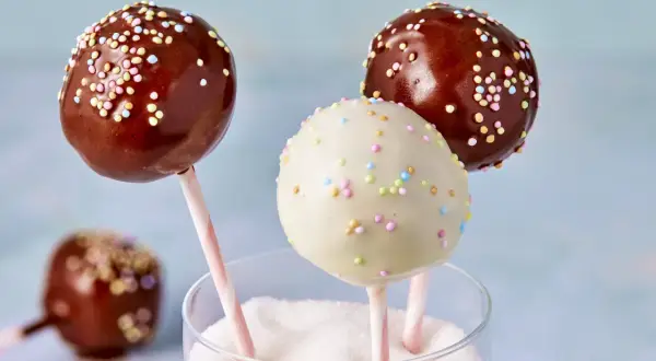 Leckere cake pops aus kuchenresten, verziert mit bunten Streuseln, stecken in einem Glas voller Zucker.