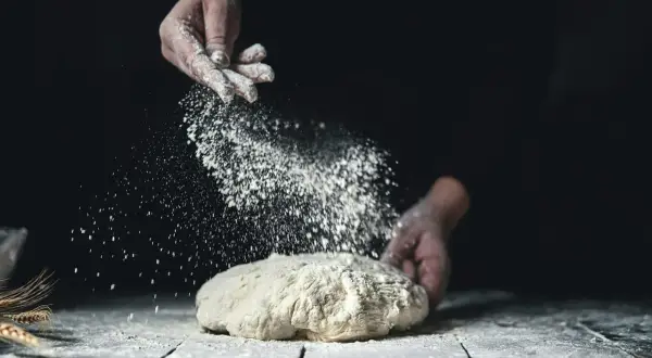 Händer strör mjöl över en deg. Det ser ut som en svensk hemmabakare som förbereder sitt bröd med fint **bread flour svenska**.