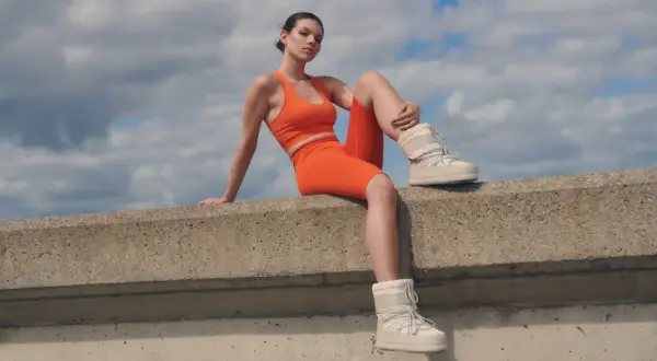 Modelka w pomarańczowym komplecie sportowym i białych śniegowcach prezentuje odważną stylizację z kolarkami.