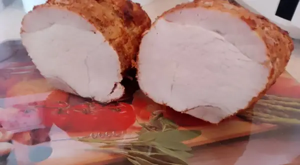 Soczysta szynka pieczona na obiad, pokrojona na pół, z chrupiącą skórką i aromatycznymi ziołami.