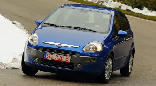 Niebieski Fiat Punto jedzie po drodze, na której widać śnieg. Z przodu widoczne są **czerwone tablice rejestracyjne** z numerem SO 320 B.