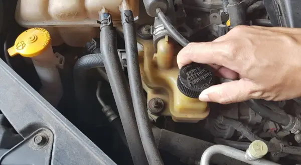 Dłoń odkręca korek zbiorniczka płynu wspomagania kierownicy. Wymiana płynu wspomagania to ważny element dbania o auto.