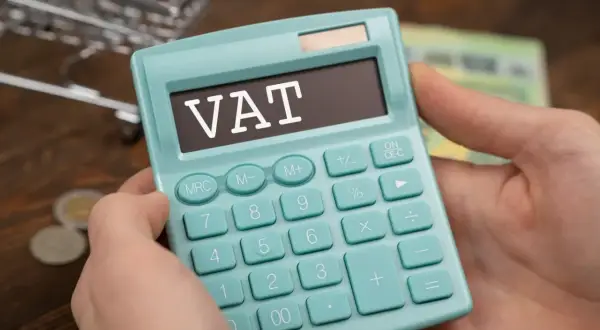 Kalkulator z napisem VAT w rękach, symbolizujący zwolnienie podmiotowe z VAT. W tle monety i banknoty.
