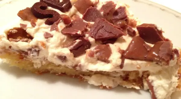 En bit krämig daim tårta med chokladbitar och en chokladdekoration.
