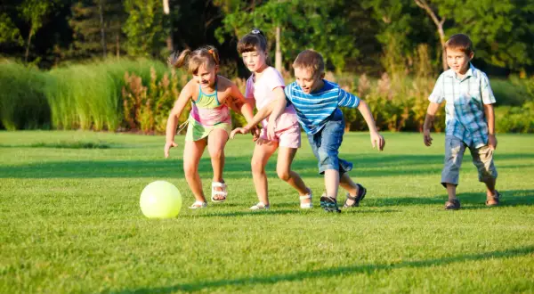 Niños jugando a la pelota en el césped, disfrutando de divertidos juegos con pelotas para niños al aire libre.