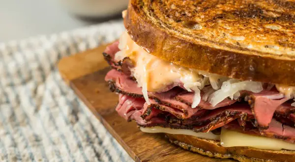 Un delicioso bocata de pastrami con pan tostado, queso fundido y chucrut.