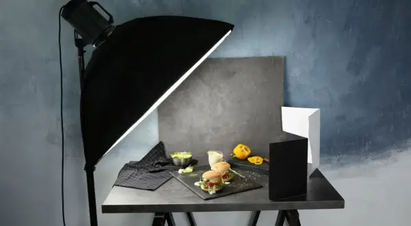 A food photography setup with burgers, salad, and a yellow pepper, illuminated by a large softbox, showcasing effective diy photography lighting.