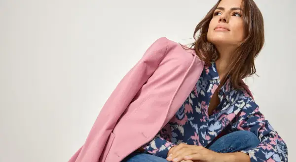 Kobieta w dżinsach i wzorzystej koszuli, narzucony różowy żakiet. Stylizacja w stylu color blocking.