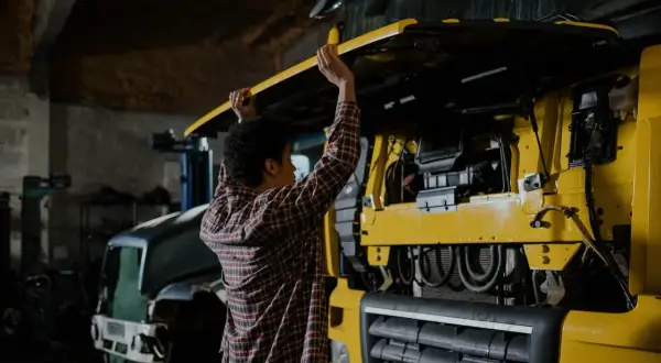 Un mécanicien examine les différentes parties d'un camion jaune, soulevant le capot pour accéder au moteur.