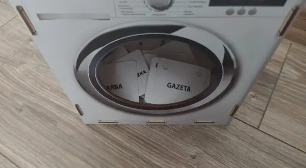Kartonowa pralka z bębnem pełnym kart z napisami "GAZETA", "ZKA", "ARBA".