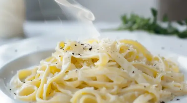 En krämig portion pasta alfredo med ånga som stiger, toppad med riven parmesan och svartpeppar.