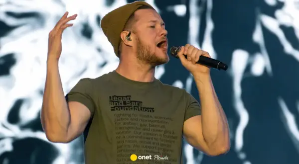 Wokalista Imagine Dragons śpiewa do mikrofonu, ubrany w zieloną koszulkę i czapkę.