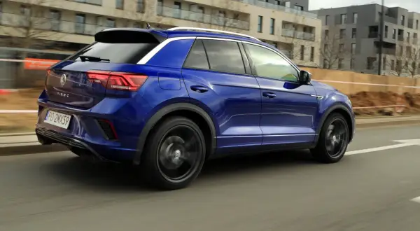 Niebieski Volkswagen T-Roc pędzi ulicą. W tle nowoczesne budynki i plac budowy.
