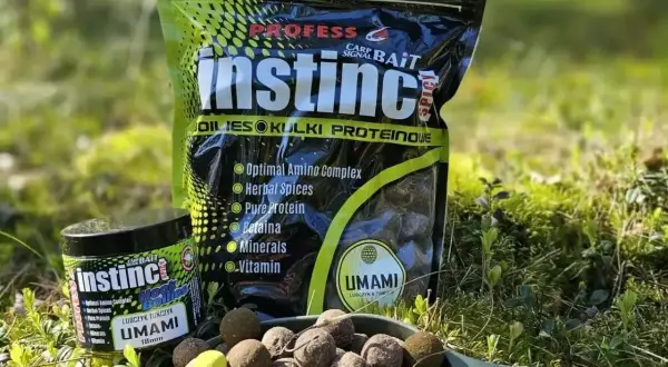 Czeskie kulki proteinowe Instinct Umami w zielonej łopatce, obok opakowania i słoiczka. Idealne na ryby!