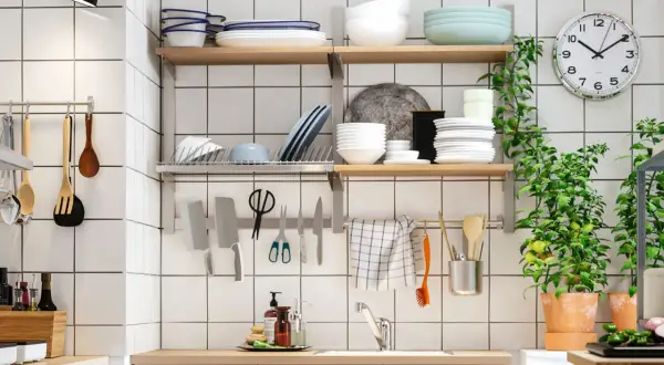 Una cocina pequeña y funcional con estantes llenos de vajilla, utensilios colgados y plantas verdes.