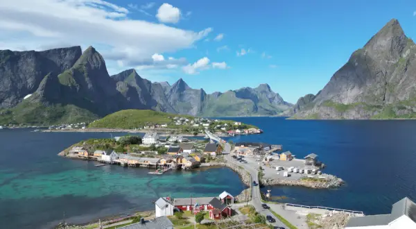 Idyllisches Dorf an der Küste mit roten und weißen Häusern, umgeben von majestätischen Bergen. Tolle Lofoten Tipps für Ihren Urlaub!