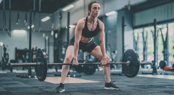 Femme concentrée en position pour un soulevé de terre, haltères lourds prêts à être soulevés dans une salle de sport.