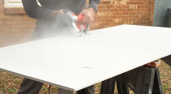 A person demonstrates how to cut cement board with a circular saw, creating a cloud of dust.