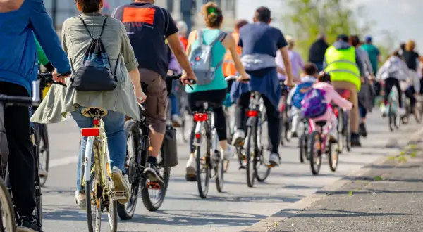 Grupa rowerzystów jedzie w kolumnie, przestrzegając przepisów. Widać plecaki i odblaskowe kamizelki.