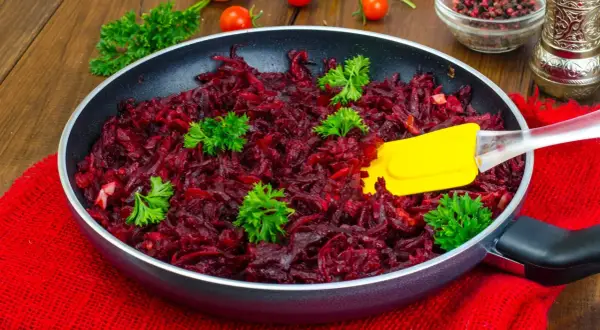 Gotowe buraczki do obiadu, pachnące i gotowe do podania. Żółta łopatka miesza aromatyczne warzywa.
