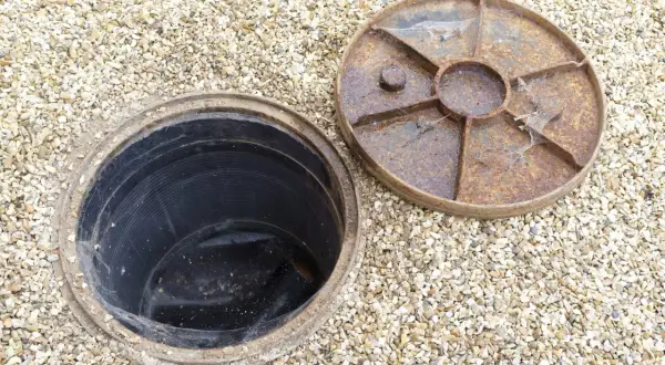 Un regard sur une canalisation d'eau pluviale ouverte, prête à être débouchée. Le couvercle rouillé est à côté.