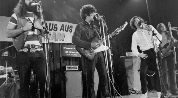 Band auf der Bühne, Gitarrist mit Afro, Sänger mit Schnurrbart, 70er Jahre Rock.