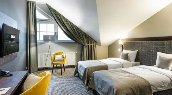 Pokój hotelowy z dwoma łóżkami, żółtym fotelem i biurkiem. Idealne miejsce na nocleg, gdzie gwiazdki w hotelach są gwarancją komfortu.