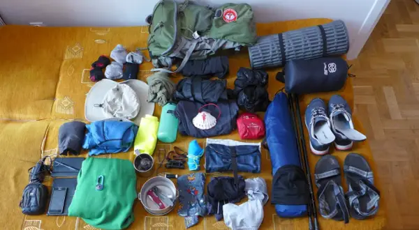 Przygotowania do camino de santiago: plecak, buty, śpiwór, karimata, ubrania, czapka, kijki i muszla pielgrzyma.