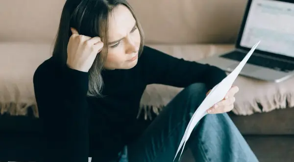Zmartwiona kobieta analizuje dokumenty, zastanawiając się, jak długo widnieje się w BIK po spłacie zadłużenia.