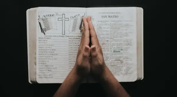 Dłonie złożone do modlitwy nad otwartą Biblią, na stronie z porównaniem Starego i Nowego Testamentu, gdzie wspomniany jest psalm 23.