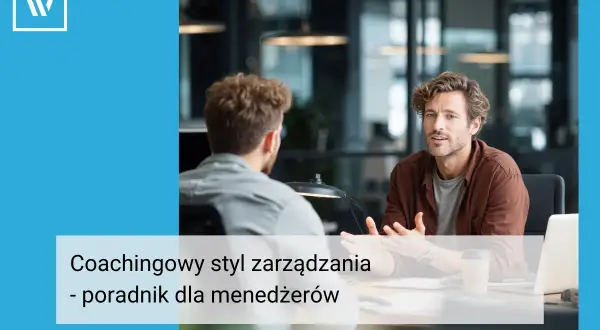 Dwóch mężczyzn rozmawia przy biurku. Jeden z nich, w brązowej koszuli, gestykuluje, wyjaśniając coś. Widać, że stosuje coachingowy styl zarządzania, wspierając pracownika.