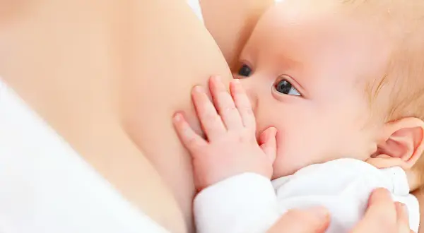 Ein Baby trinkt an der Brust. Die Hand des Babys ruht auf der Brust, was die Milchproduktion anregen kann.
