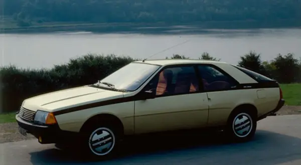 Złoty Renault Fuego z czarnymi pasami na boku, zaparkowany nad jeziorem.
