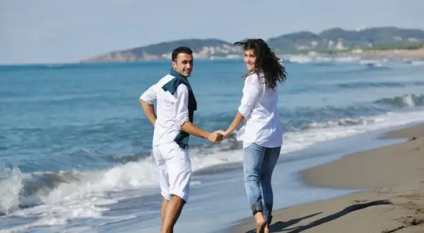 Para na plaży, trzymając się za ręce, cieszy się majówką. Słońce, morze i góry w tle tworzą idealny krajobraz.