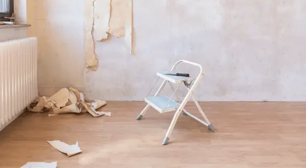 Tapete entfernen ist zeitaufwendig. Ein kleiner Tritt, Werkzeug und Tapetenreste liegen auf dem Holzboden.