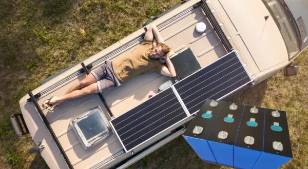 Mężczyzna odpoczywa na dachu kampera z panelami słonecznymi, obok magazyn energii 15 kWh.